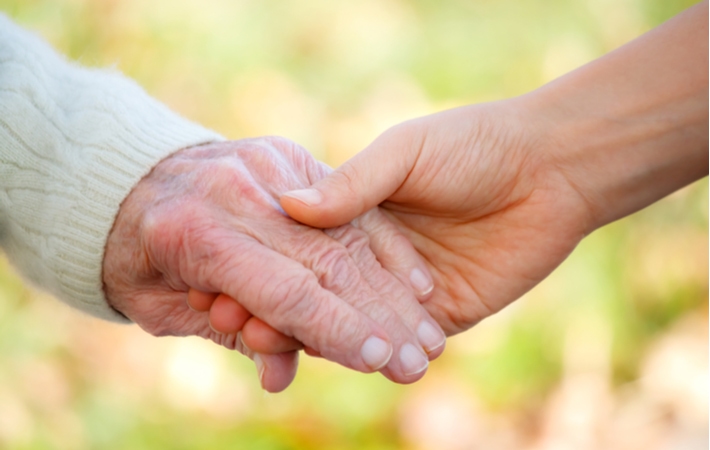 A young personing holding the hand of a senior showing the concept of support for the elderly in a senior living community