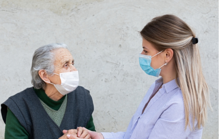 A female caregiver holding the hands of a senior woman in a senior living community while they have a conversation