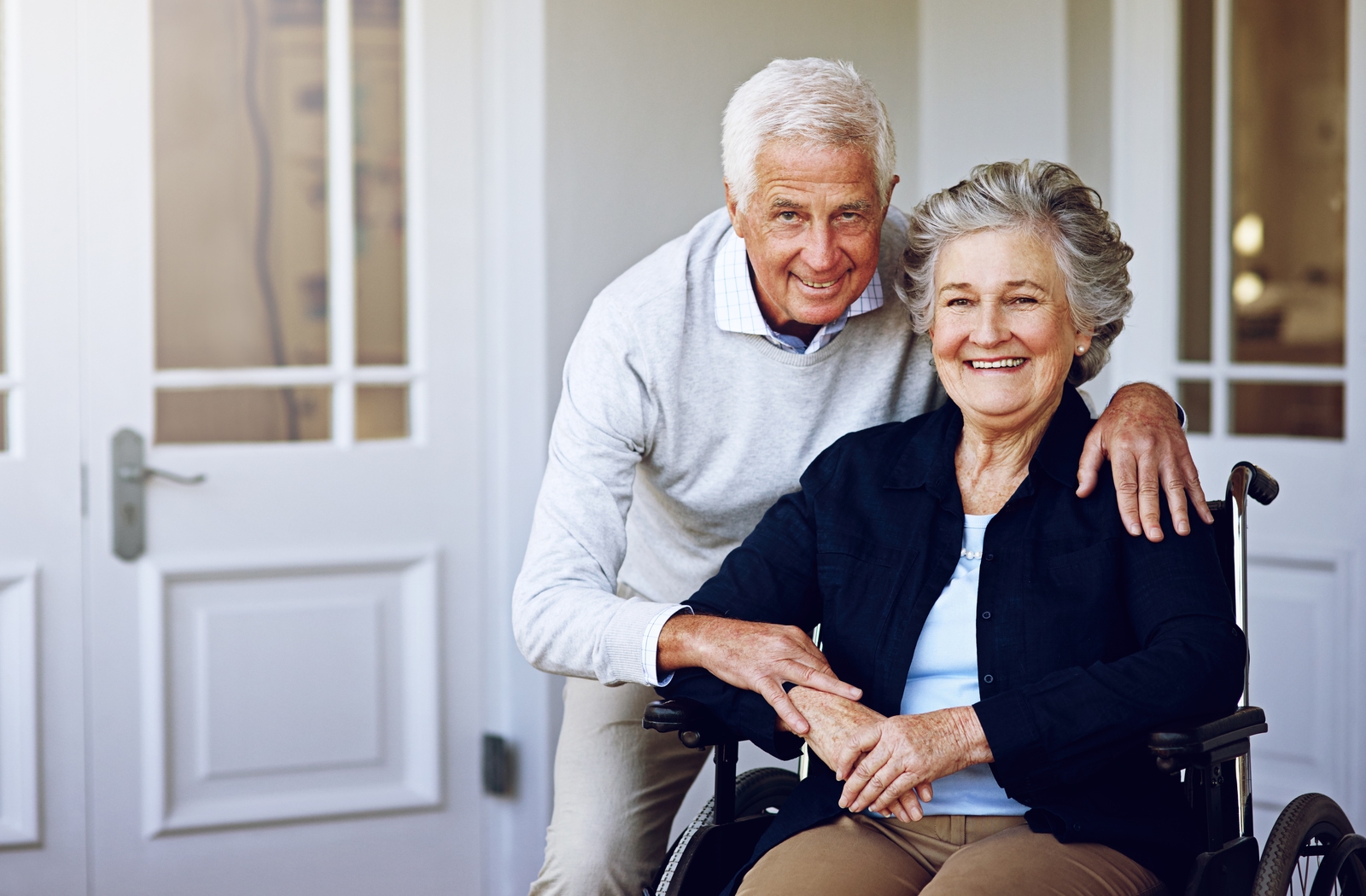 A senior couple, the woman in a wheelchair, standing outside of the door to their senior living community