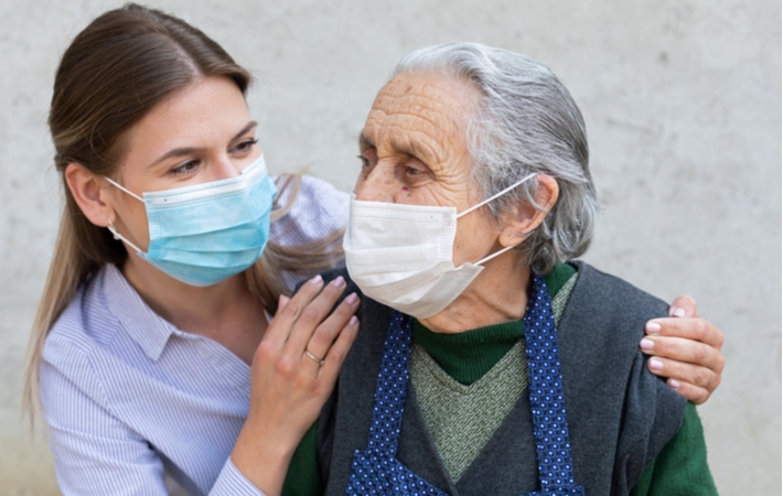 A female caregiver talking to a senior woman with her arms on her shoulders