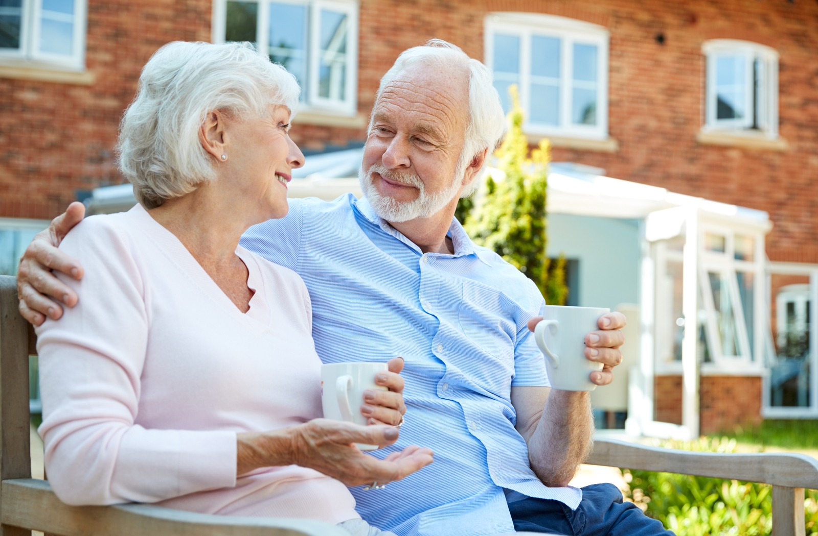 A senior couple sitting outside drinking coffee in the courtyard of their senior living community