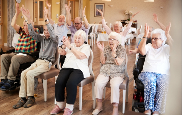 A group of seniors in a retirement community all seated raising their arms in the air