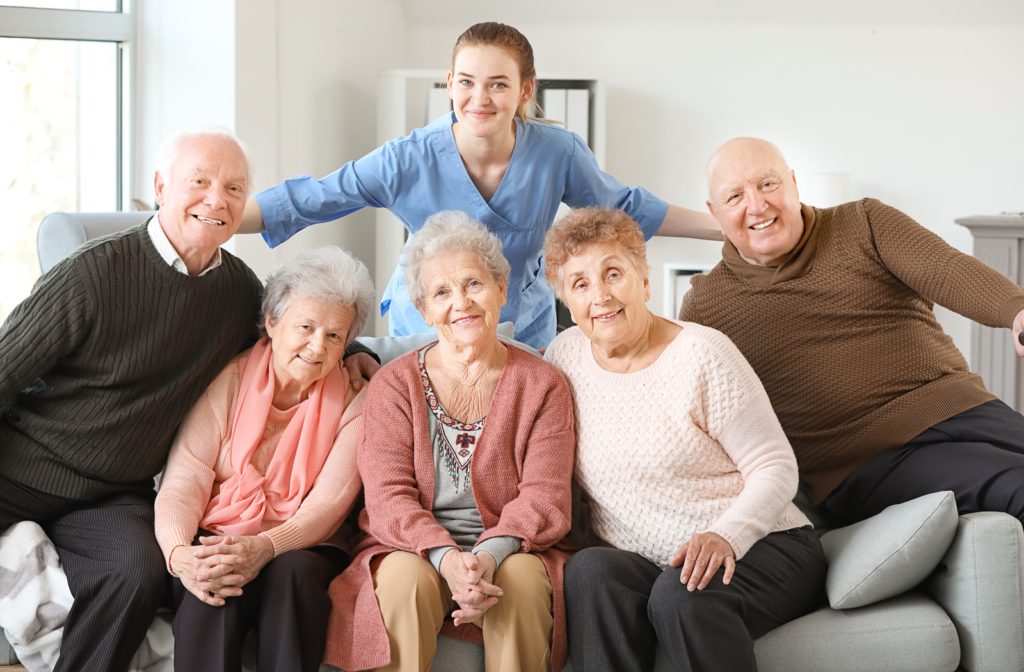 A group of residents in a senior living community with a caregiver smiling just behind