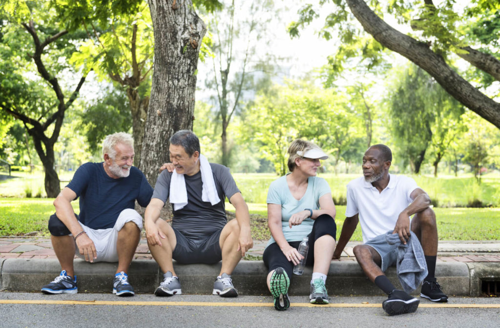 A group of four adults are sitting on a curb after their morning jogging activity.