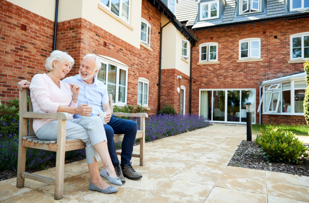  "A senior couple sitting on a bench outdoors and drinking coffee in a senior living community."