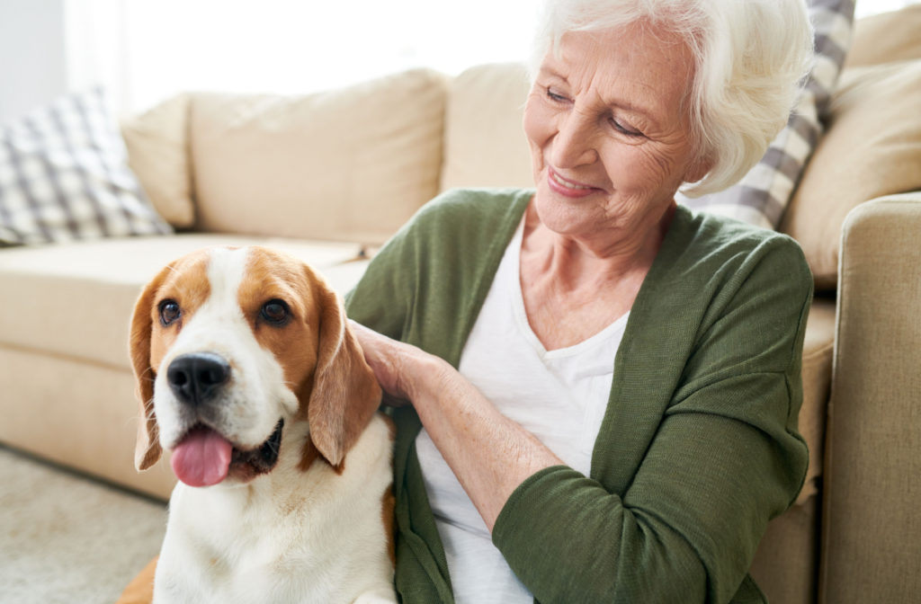 A senior woman happily petting her pet dog who has a very relaxed look.